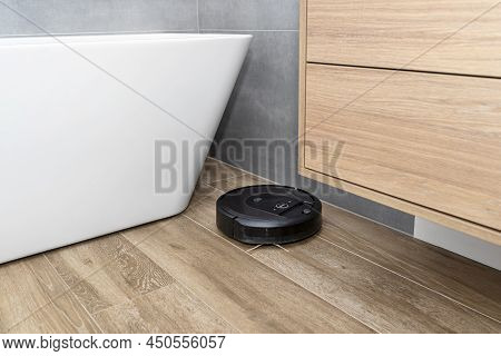 A Modern Robotic Vacuum Cleaner Cleans The Ceramic Tiles In The Bathroom Next To The Bath, An Autono