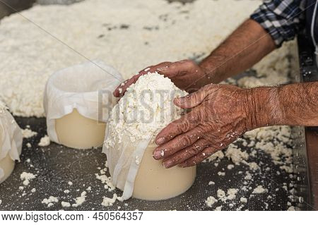 Close-up Of An Old Mans Hands Finishing Filling A Large Fresh Cheese Mould With Curd.