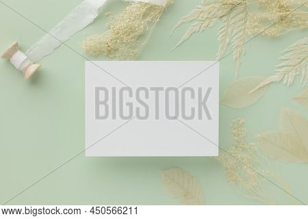 Blank Greeting Card Invitation Mockup 5x7 On Brown Envelope With Dried Flowers On Pastel Green Backg