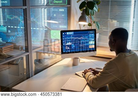 Rear View Of African Programmer Sitting At His Workplace In Front Of Computer And Working With Graph