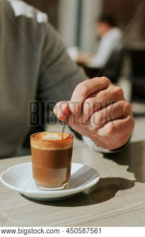 closeup of a young caucasian man stirring his machiatto with a spoon sitting at the table of a sidewalk cafe