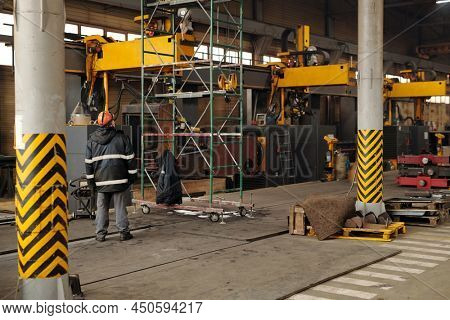 Worker of large industrial plant standing in front of technical construction and part of huge machie while working in warehouse