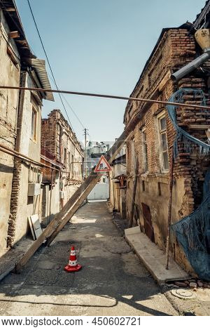 Old collapsing buildings with wooden supports and warning road sign in Tbilisi, Georgia. The atmosphere of the old city of Tiflis. Old dilapidated brick houses.
