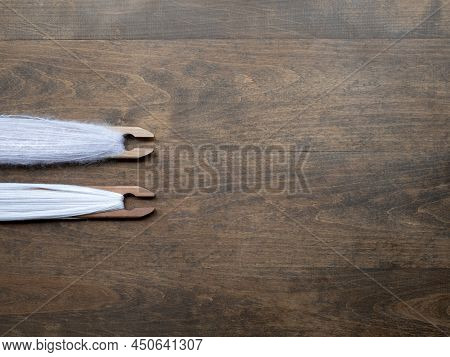 Brown Wooden Background With Two Weaving Shuttles Full Of Light Pink Yarn, Copy Space. Concept Of Cr
