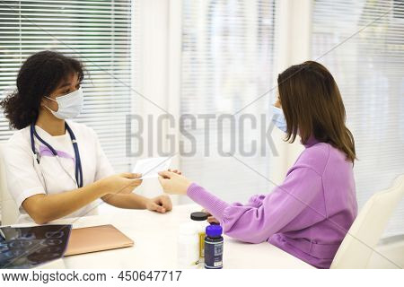 African-american Woman Doctor Wearing Face Mask Giving Cd With X-ray Image To Female Patient During 
