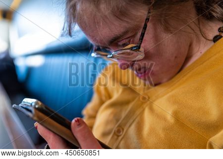 Indoor Portrait Of A 39 Year Old White Woman With The Down Syndrome, Sitting With A Smartphone In He