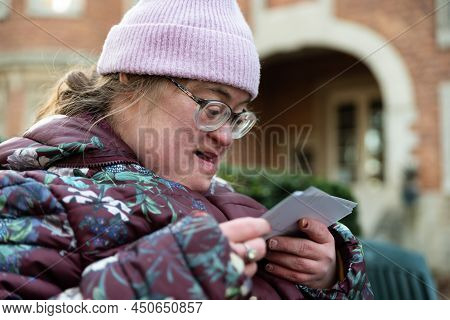 Outdoor Portrait Of A 39 Year Old White Woman With The Down Syndrome Looking At Printed Pictures