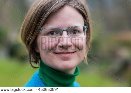 Close Up Portrait Of A Young White Woman With Glasses Wearing A Blue And Green Sweater With A Green 