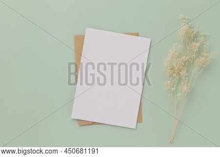 Blank Greeting Card Invitation Mockup 5x7 On Brown Envelope With Dried Flowers On Pastel Green Backg