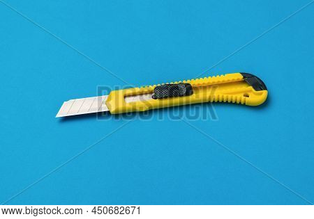 Yellow And Black Stationery Paper Knife On A Bright Blue Background. Minimalistic Concept.