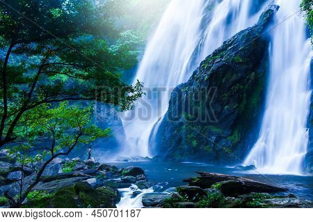 An Asian Barechested Man Stands On The Rock And Looks At The Great Waterfall In Rain Season. Khlong 