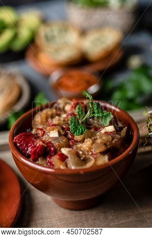 closeup of an earthenware bowl with some escalivada, a side dish made with roasted eggplant, onions and red pepper typical of catalonia, spain, on a table with some other food dishes