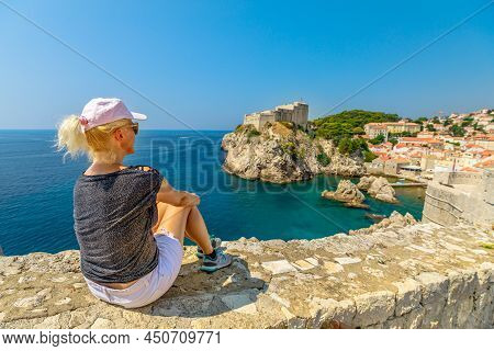 Woman Resting On Top Walls Of Dubrovnik City Of Croatia. Looking Fort Lovrijenac Fortress, Over The 