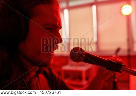 Partial Image Of Emotional Male Singer Singing Song In Microphone At Blurred Red Home. Concept Of Do