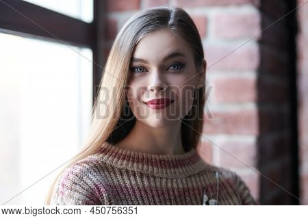 Attractive girl in stylish casial clothes stands by the window in a loft room and happily smiles. Happy and successful people. 