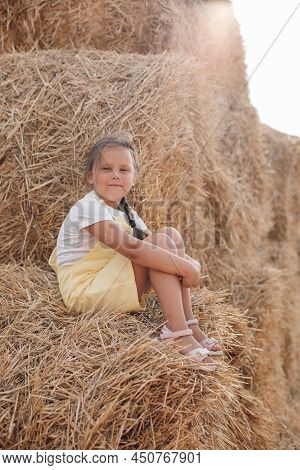 Portrait Of Peaceful Pretty Young Girl On Hayrick With Smile And Squinted Eyes Looking At Camera And