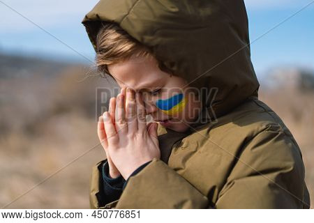 Ukrainian Boy Closed Her Eyes And Praying To Stop The War In Ukraine. Hands Folded In Prayer Concept
