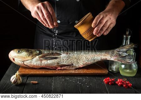 Cook Prepares Silver Carp Herring In The Restaurant Kitchen. The Cook Sprinkles Salt On The Fish. Wo