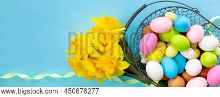 Basket With Easter Eggs And Bouquet Of Yellow Narcissus On Blue Paper Background. Flat Lay  Top View
