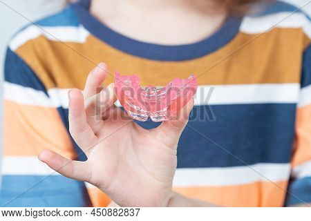 Cute Little Caucasian Girl With Blond Hair Is Holding A Pink Dental Myofunctional Trainer On White T