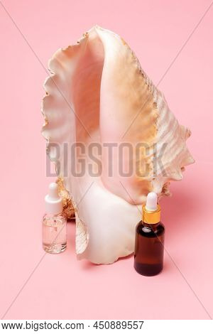 Transparent And Brown Cosmetic Bottles With Dropper On A Pink Background With Decor Of Strombus Giga