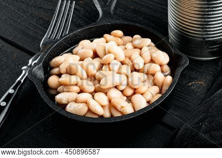 White Canned Beans Set, With Metal Can, In Cast Iron Frying Pan, On Black Wooden Table Background