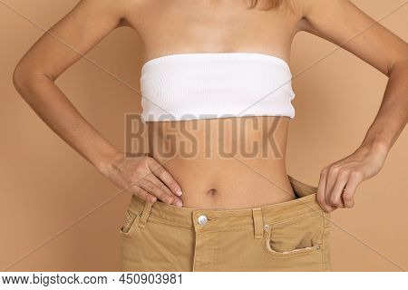 Woman In White Bra And Large Cream Colored Jeans Showing Thin Waist On Flesh Background. Healthy Eat