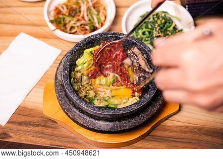 Bibimbap In A Black Heated Stone Bowl, Korean Traditional Dish- Bibimbap Mixed Rice With Vegetables 