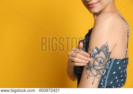 Woman Applying Cream Onto Her Arm With Tattoo On Yellow Background, Closeup. Space For Text