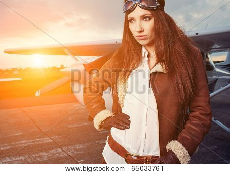 Portrait of young beautiful woman pilot in front of airplane.