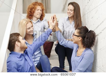 business, office, gesture and startup concept - smiling creative team doing high five gesture sitting on staircase