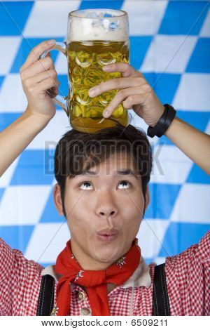 Uomo asiatico avendo Oktoberfest Beer Stein la testa e guarda sorpreso