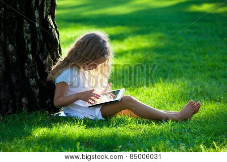 Child with tablet pc outdoors. Little girl on grass with computer