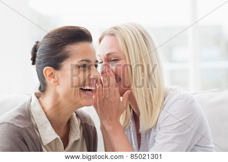 Woman revealing secret to her friend smiling and sitting on sofa