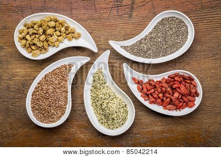 superfood samples  (mulberry, chia seeds, hemp seeds, goji berry, flax seed) in teardrop shaped bowls against grunge wood