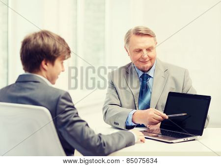 business, advertisement, technology and office concept - older man and young man with laptop computer in office