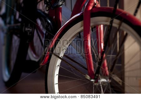 Close up of the front of a red bicycle with whitewall tires leaning against a carport wall, tilt-shift soft focus filter.
