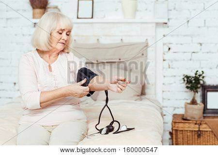 Check it out. Pleasant elderly moody woamn sitting in bed and measuring blood pressure