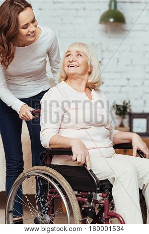 Show appreciation. Pleasant young caring woman taking care of her grandmother who is sitting in wheelchair