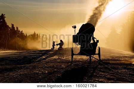 Father is playing with his children next to the snow cannon.