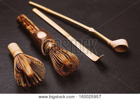 Two chasens - special bamboo whisk and two bamboo spoons for matcha tea. Special accessories for japanese matcha, lying on black textured stone background.