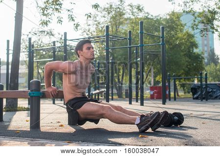 Young fit man doing triceps dips exercises during outdoor cross training workout. Fitness male model