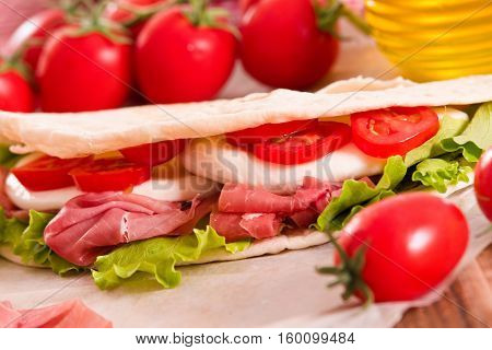 Piadina with ham and lettuce on wooden table.