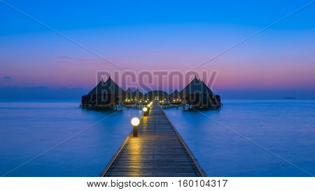 Gorgeous sunset over the ocean. Splash of waves on the white sand beach. Panorama of tropical island Beach with оverwater bungalows
