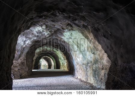 Тunnel in the mountain with a footpath stretching into the distance. Diminishing perspective. Interesting structure and color of the stone.