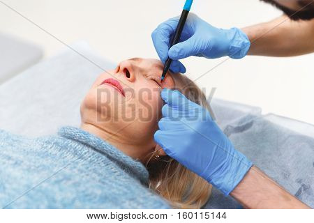 marking the face of an elderly woman old of plastic surgery at a reception at the doctor