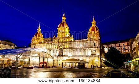 Night cityscape of Coruna, Galicia, Spain. Illuminated Municipal Palace and City Hall Square of Coruna at blue evening hour