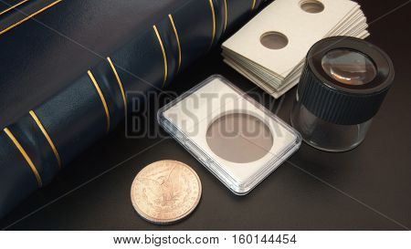 Old American silver dollar on black table with magnifying glass, numismatic supplies and album for coins - Numismatic scene