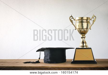 graduation cap with champion golden trophy on wood table with copy space ready for your design.graduation success education concept