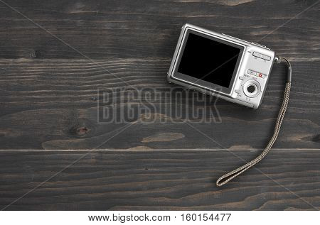 back silver digital compact camera with blank black screen display and hand strap on black vintage wood table top view with copy space included clipping path for compact camera black screen display